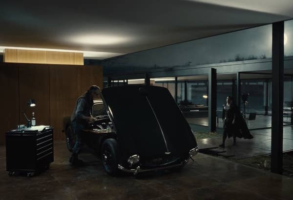 Alfred working on a car as Superman walks up