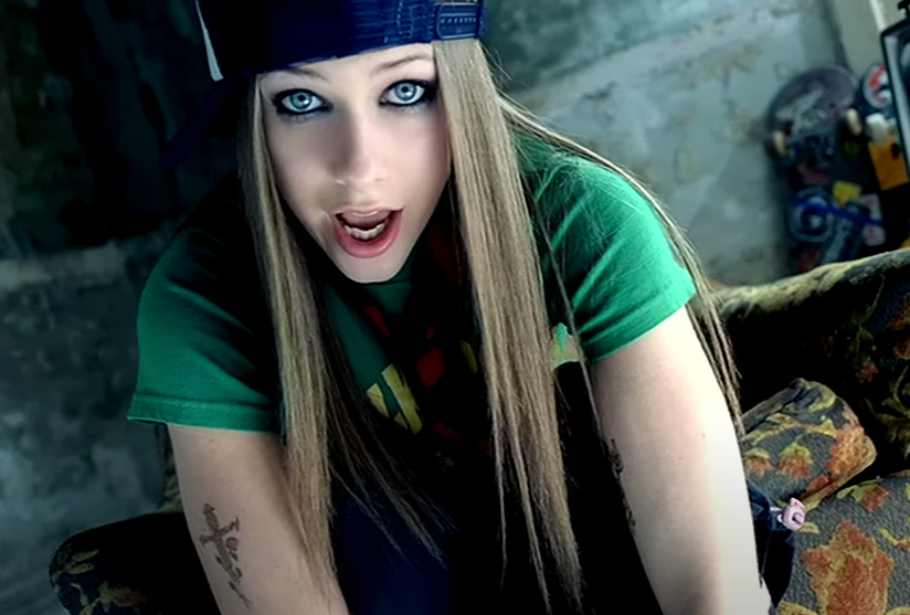 Screenshot of Avril in a green T-shirt and backwards cap from the Sk8er Boi video