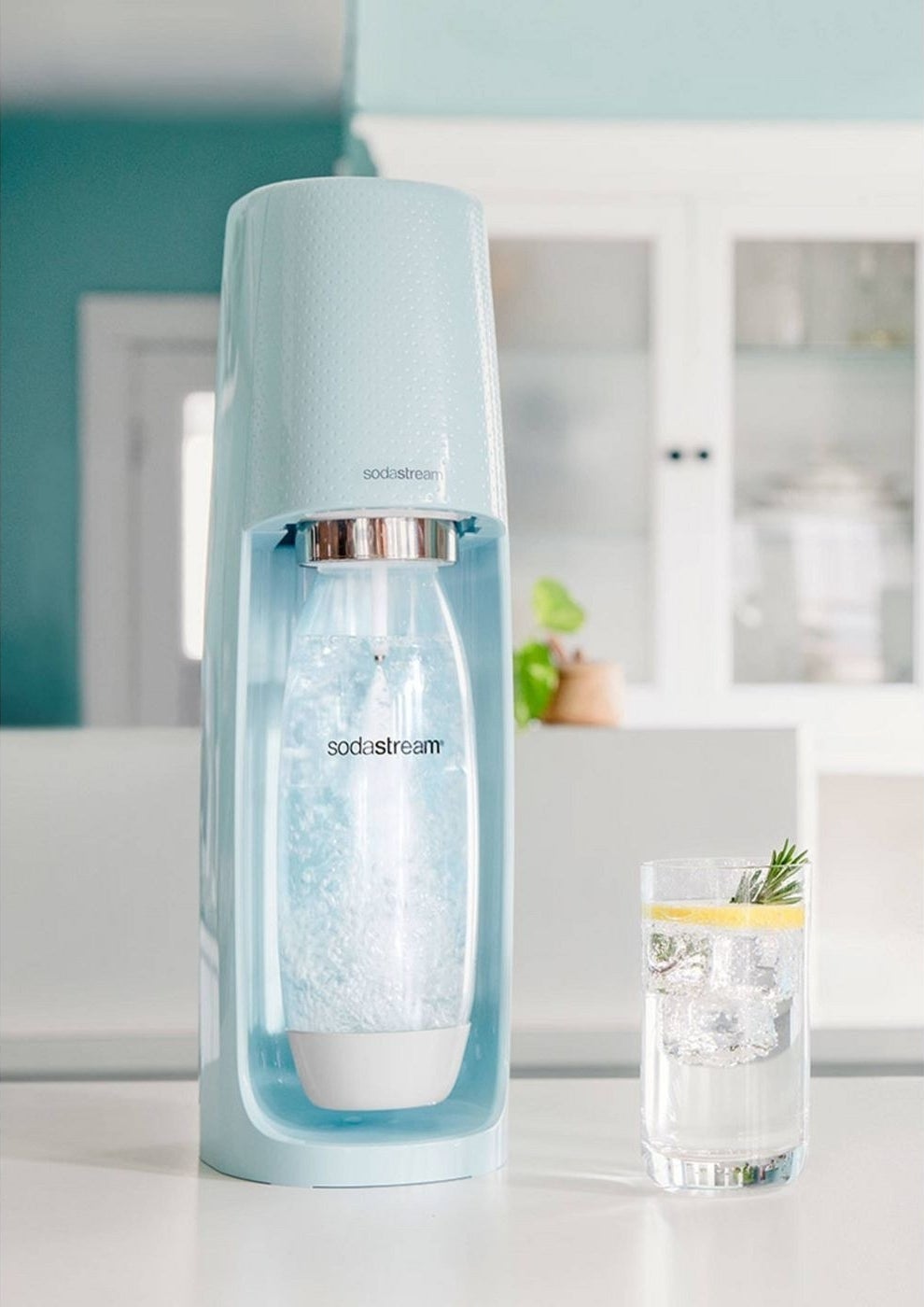 light blue sodastream making sparkling water on a counter, next to a glass
