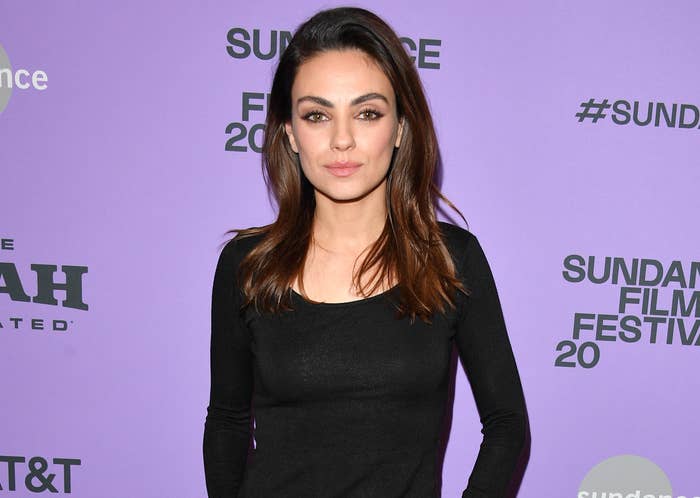 Mila wears a black stop while walking a red carpet at an event