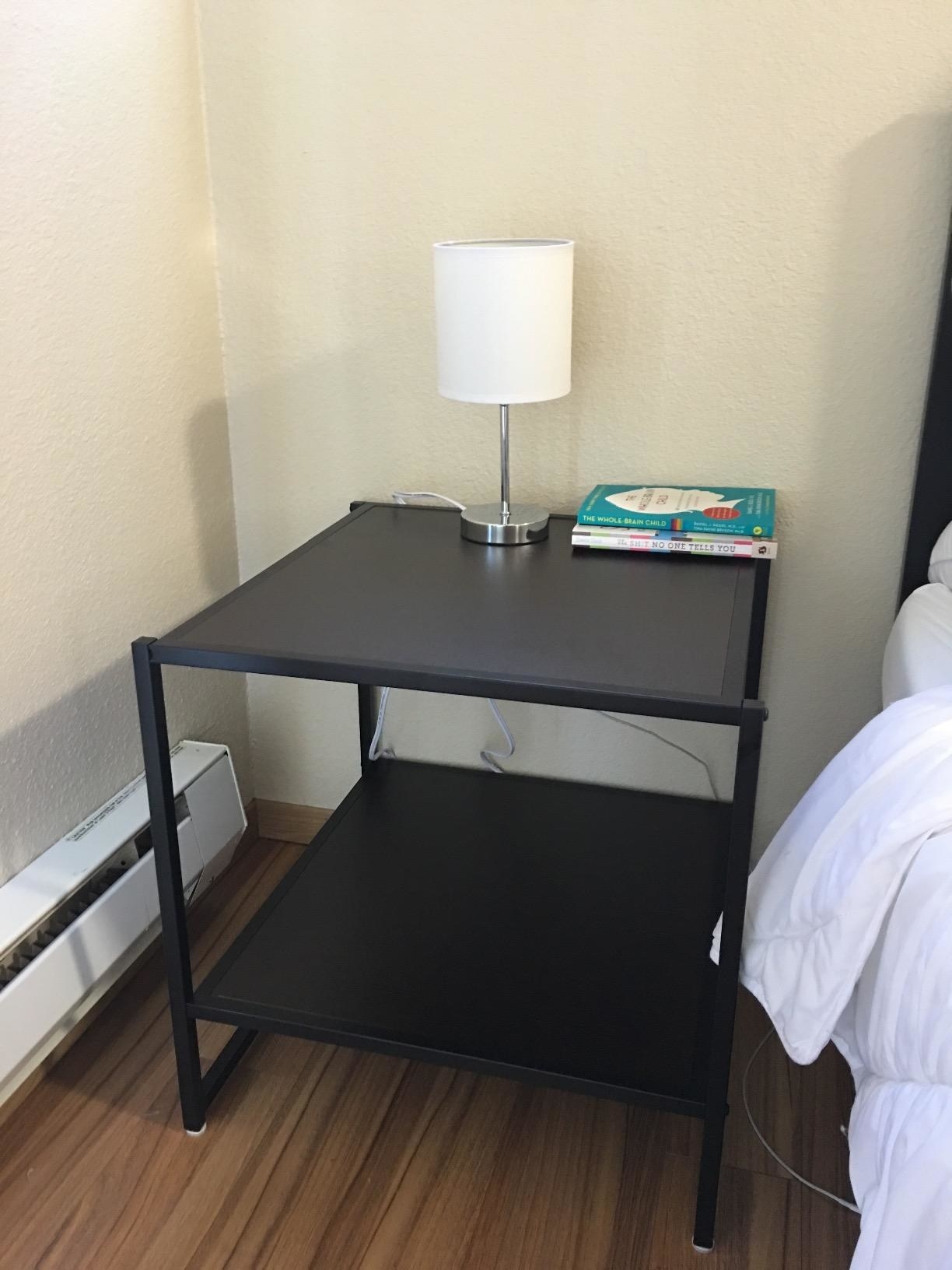 The nightstand, which is rectangular and open, with one shelf and a flat top surface
