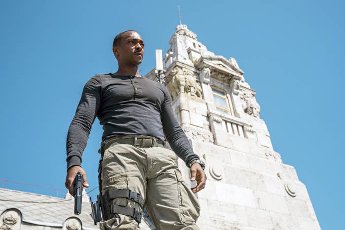 anthony mackie standing outside holding a gun in one hand