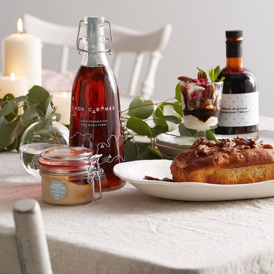 A glass bottle of maple syrup on a table with a small loaf of bread