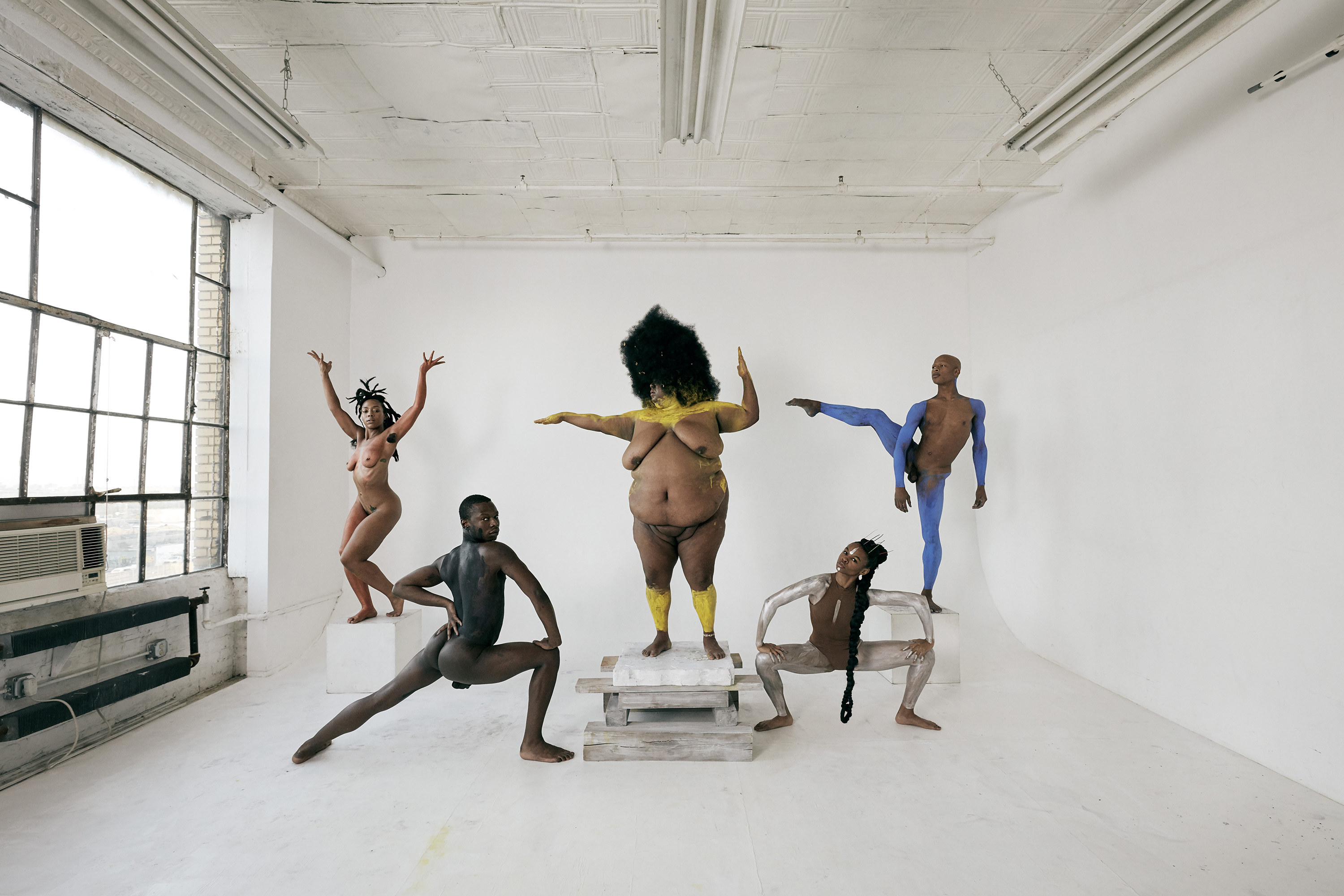 five naked dancers with their bodies painted in a white room, posing for the camera
