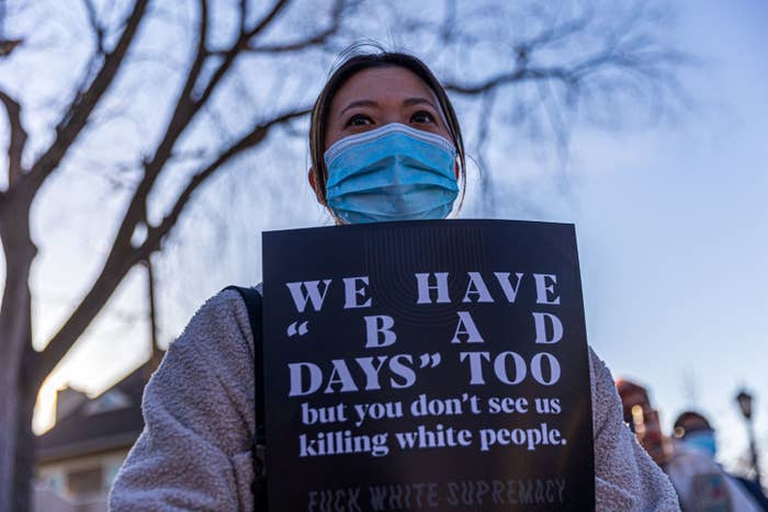 An Asian American woman stands in a medical mask at a protest with a sign that says, &quot;We have &#x27;bad days&#x27; too but you don&#x27;t see us killing white people. Fuck white supremacy.&quot;