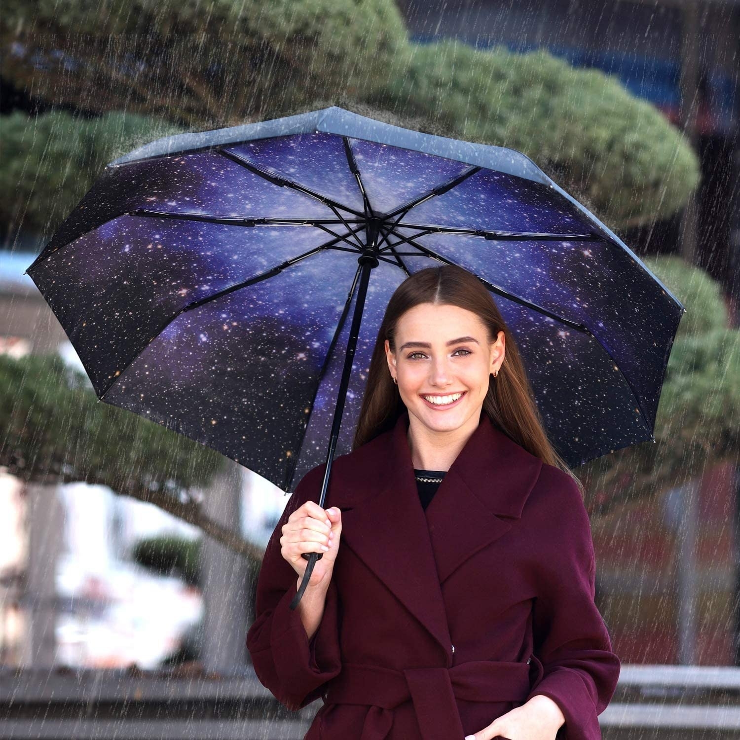 A smiling person holding an umbrella in the rain