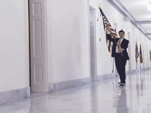 Stephen Colbert skateboarding down a hallway while waving a US flag