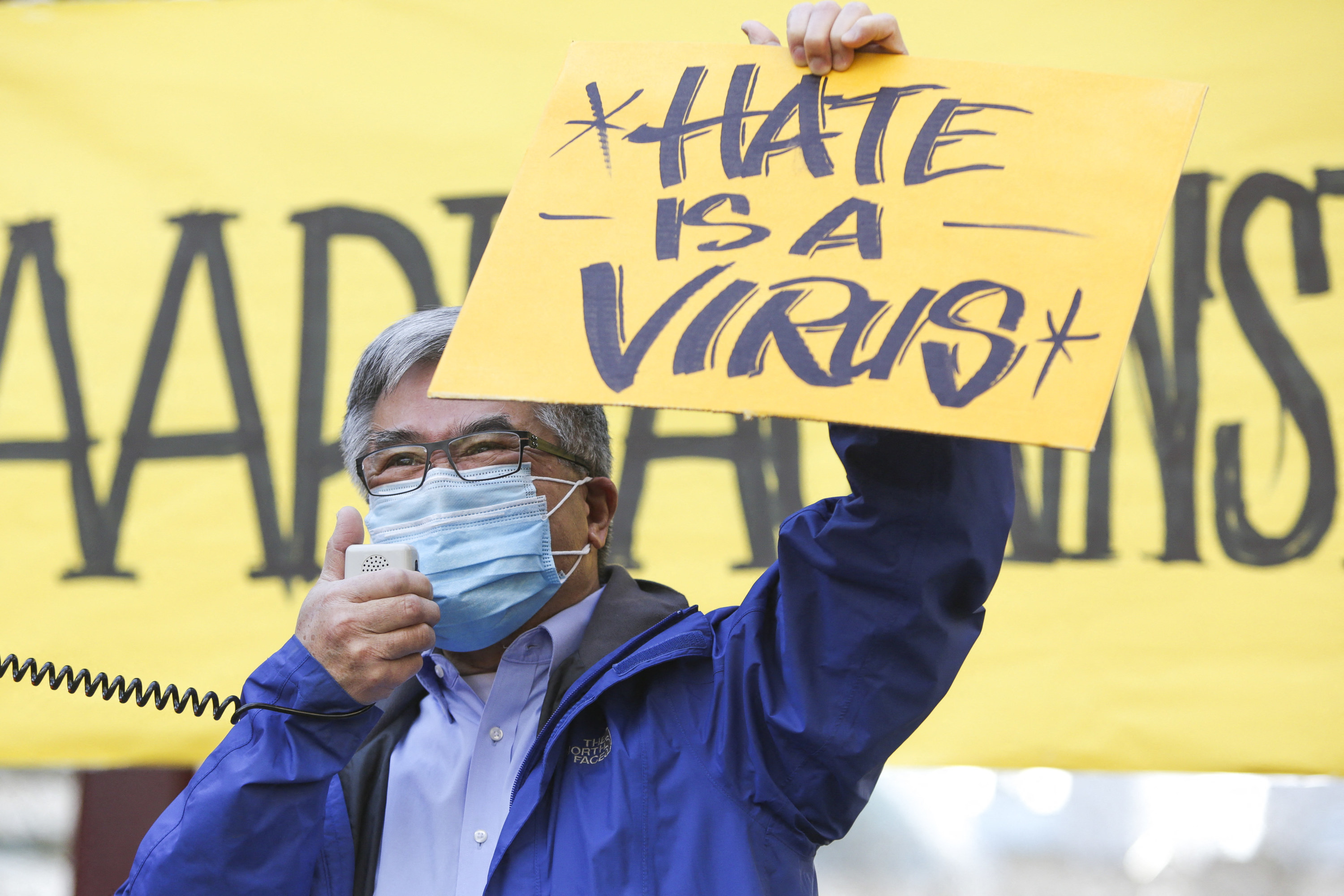 The former governor of Washington, Asian American Gary Locke, speaks at a rally in Seattle in a medical mask while holding a sign that says, &quot;Hate is a virus&quot;