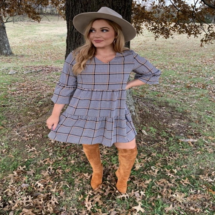 a reviewer wearing the plaid long-sleeve dress with a hat and boots