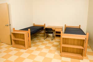 An empty dorm room with two twin beds and a desk with a chair in between
