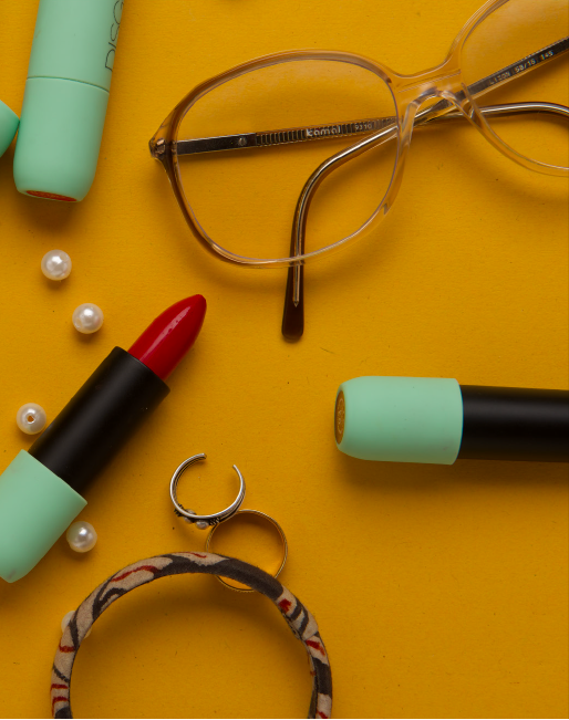 A flatlay of lipsticks, rings, pearls, and a pair of glasses