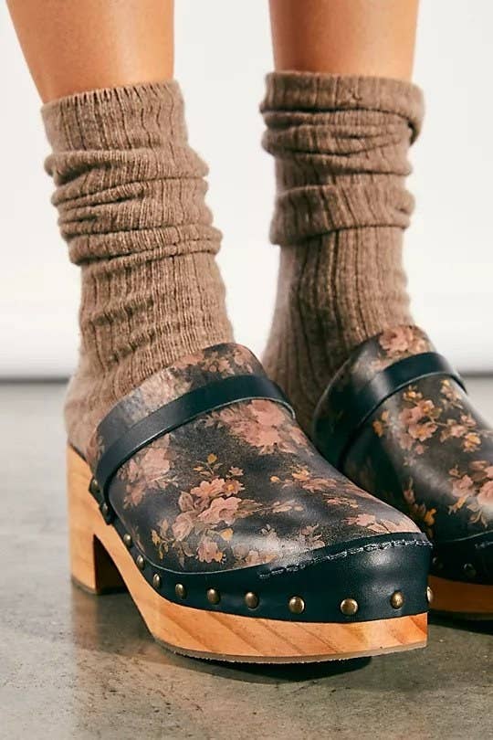 Black leather clogs with wooden base and heels. They have metal studs and a floral pattern on top. 