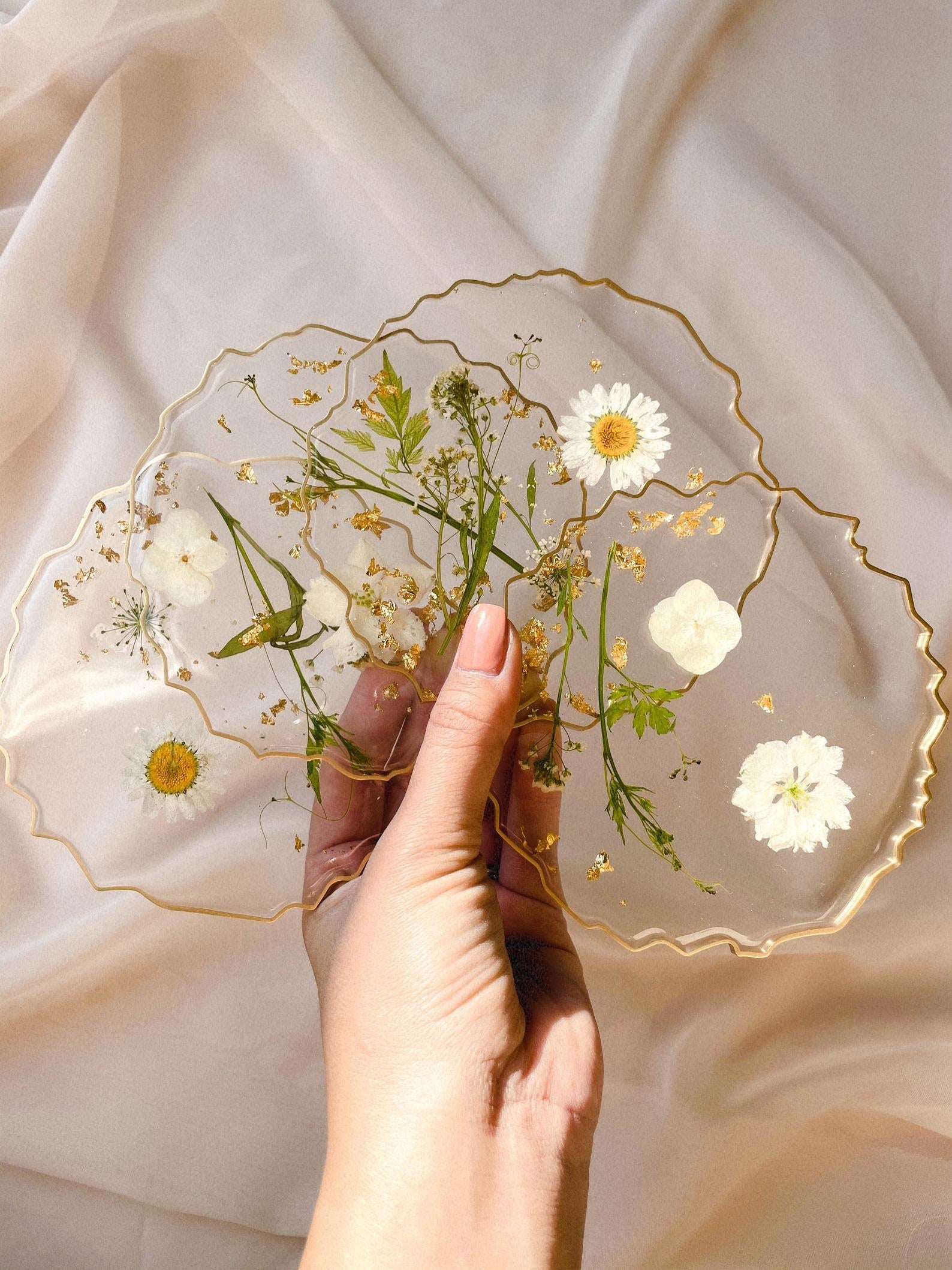 Set of transparent coasters with uneven edged gold rim and white pressed flowers inside 