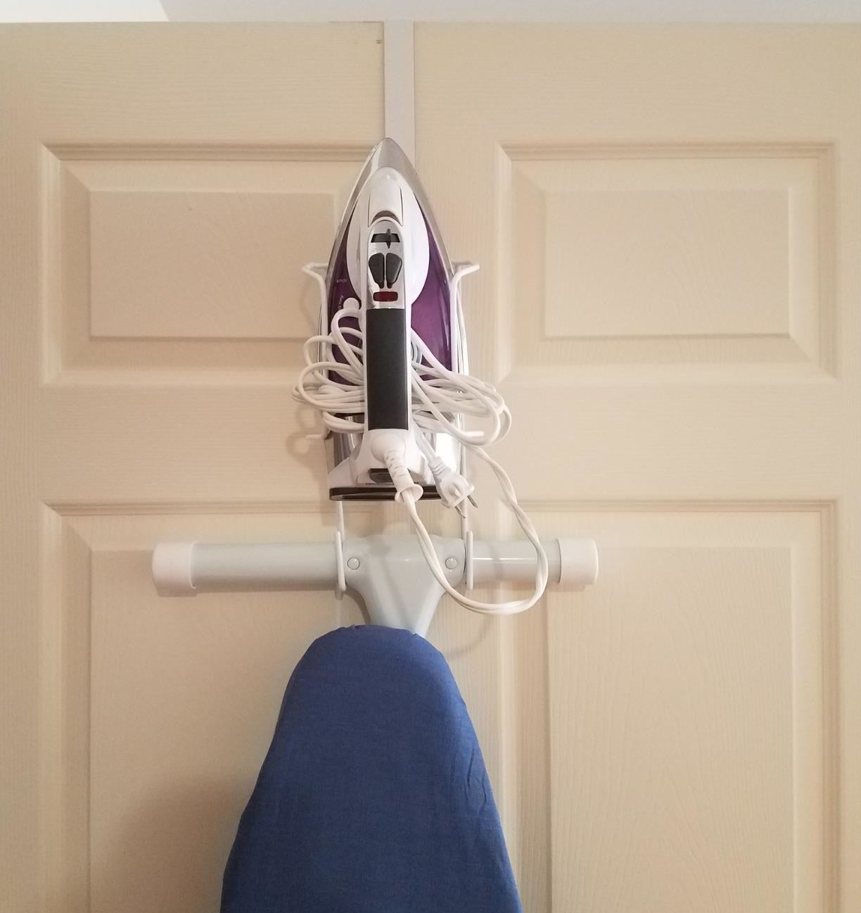 reviewer photo showing their ironing board and iron perfectly stored on the over-door organizer 