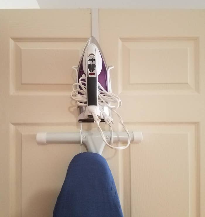 reviewer photo showing their ironing board and iron perfectly stored on the over-door organizer 