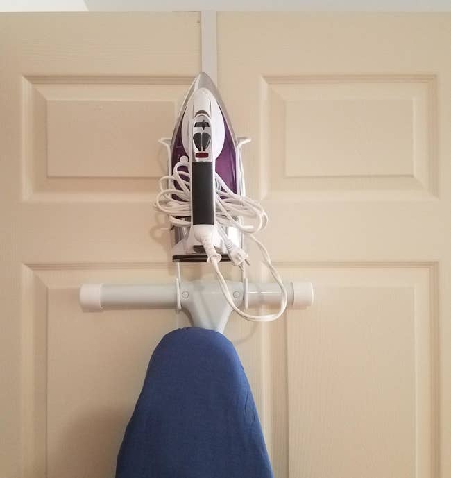 reviewer showing their ironing board and iron perfectly stored on the over-door organizer