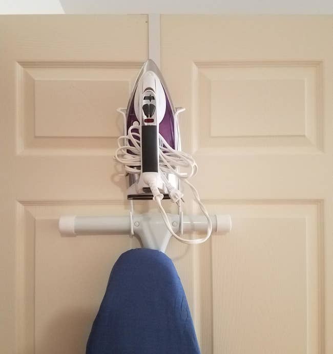 reviewer showing their ironing board and iron perfectly stored on the over-door organizer
