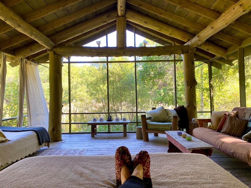 the inside of the Airbnb with a massive window overlooking a forest 