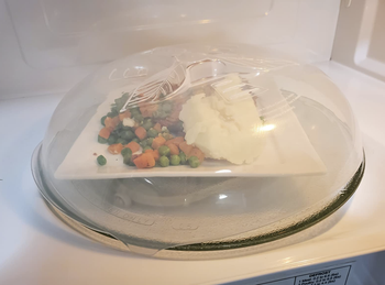 reviewer covering plate of food in microwave with splatter cover