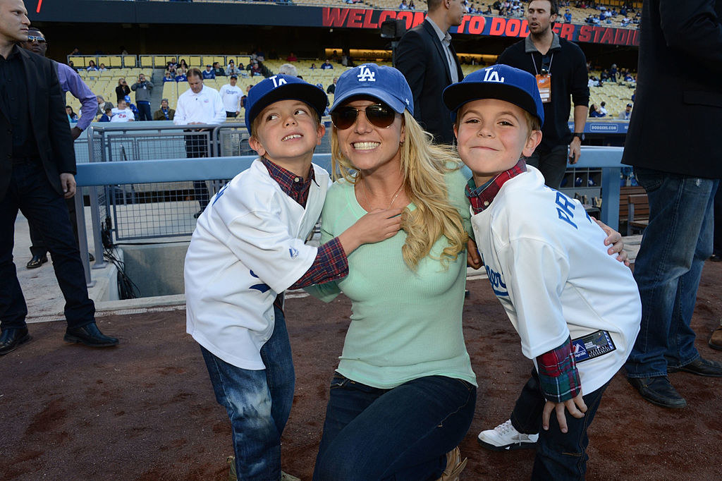 Britney leaning down to pose with her sons who are wearing Dodgers jerseys and baseball caps