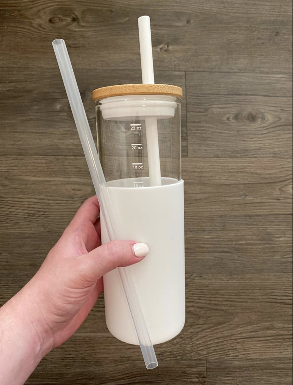 Glass water bottle with measurements on the side and a bamboo lid with a straw plus white protective sleeve on the bottom