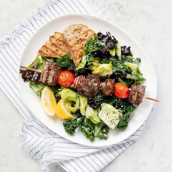 A plate of kale caesar salad topped with beef cube skewers