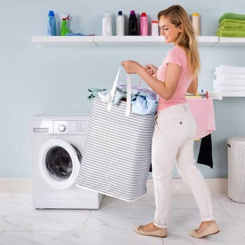 Model holding large square-bottomed laundry hamper with white and blue stripes by the side handles 