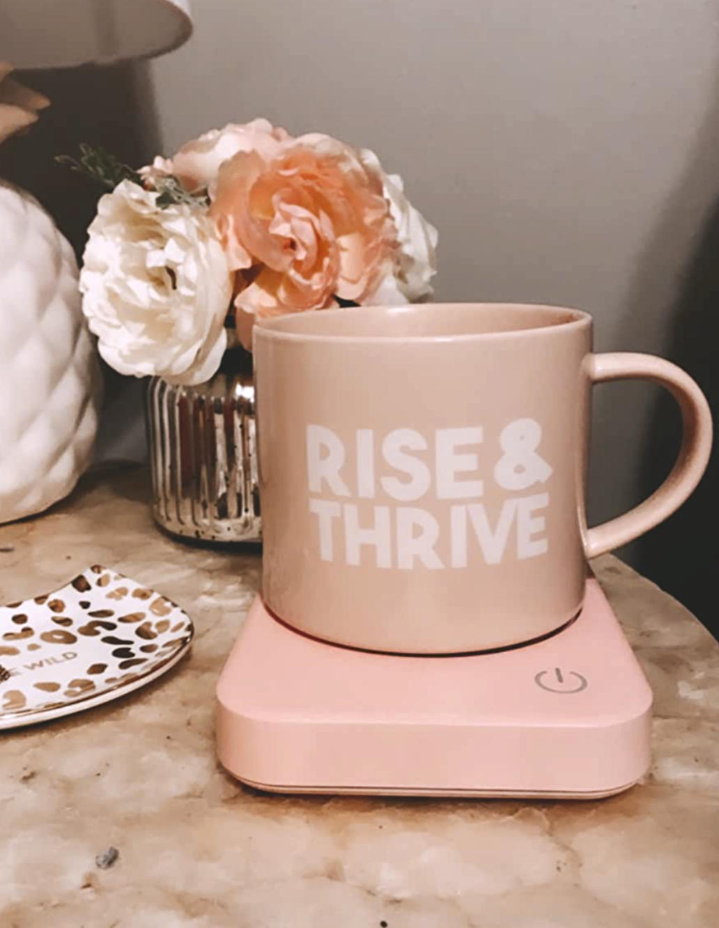 A pink mug of coffee that says &quot;Rise &amp;amp; thrive&quot; sitting on top of a pink heated small plate 