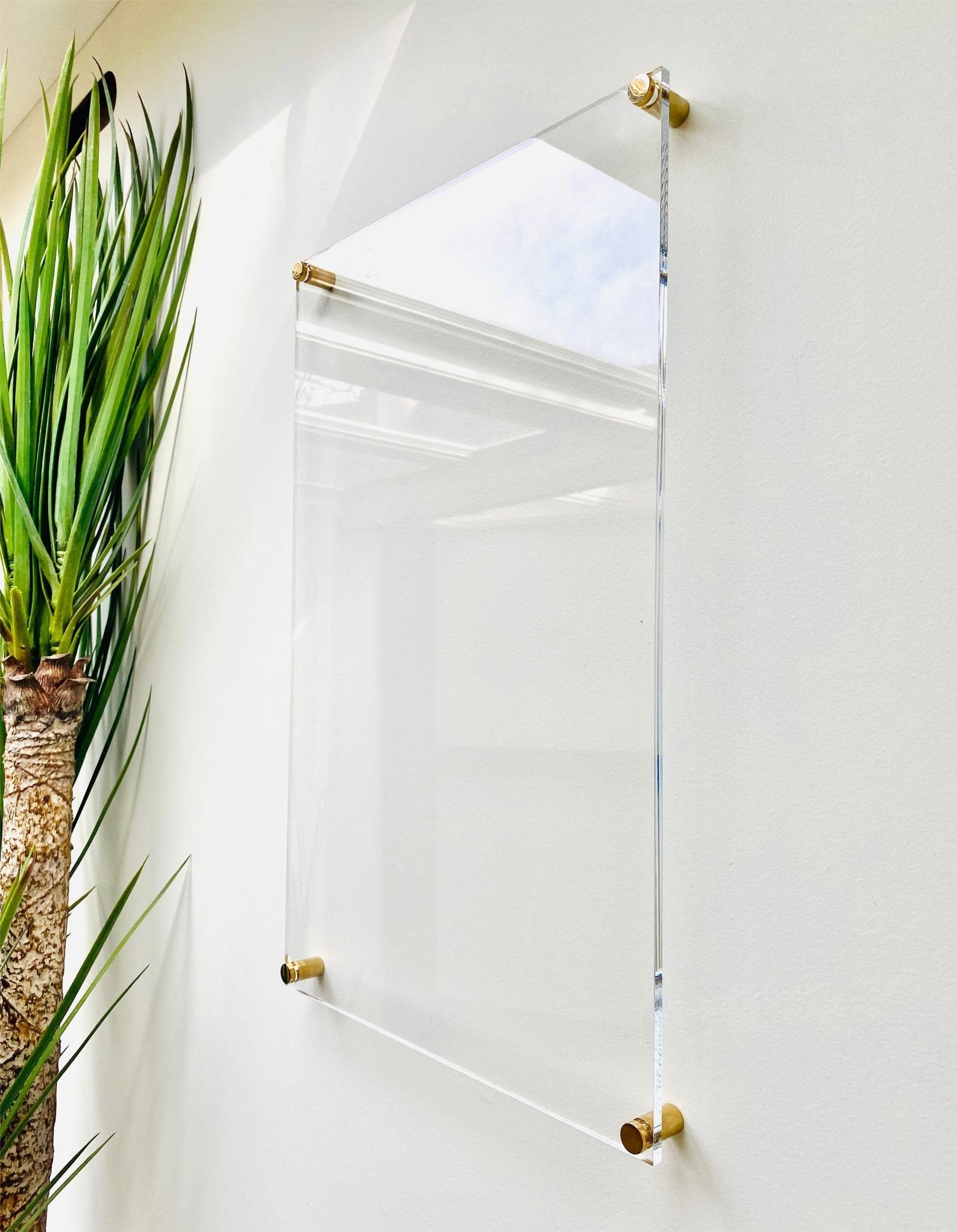 Square transparent whiteboard with four gold knobs installed on a wall 