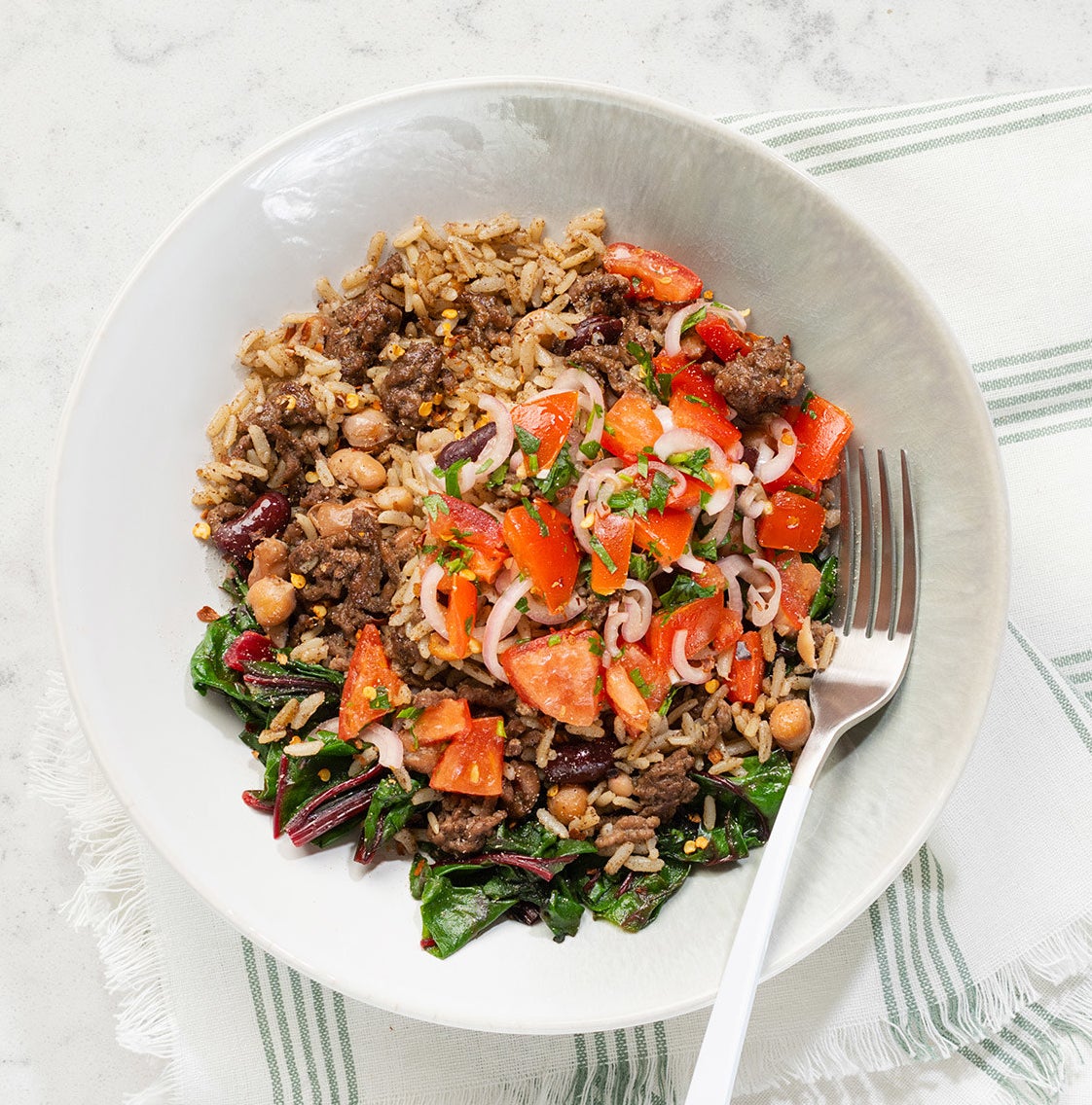 A beef rice bowl on a marble counter next to a tea towel