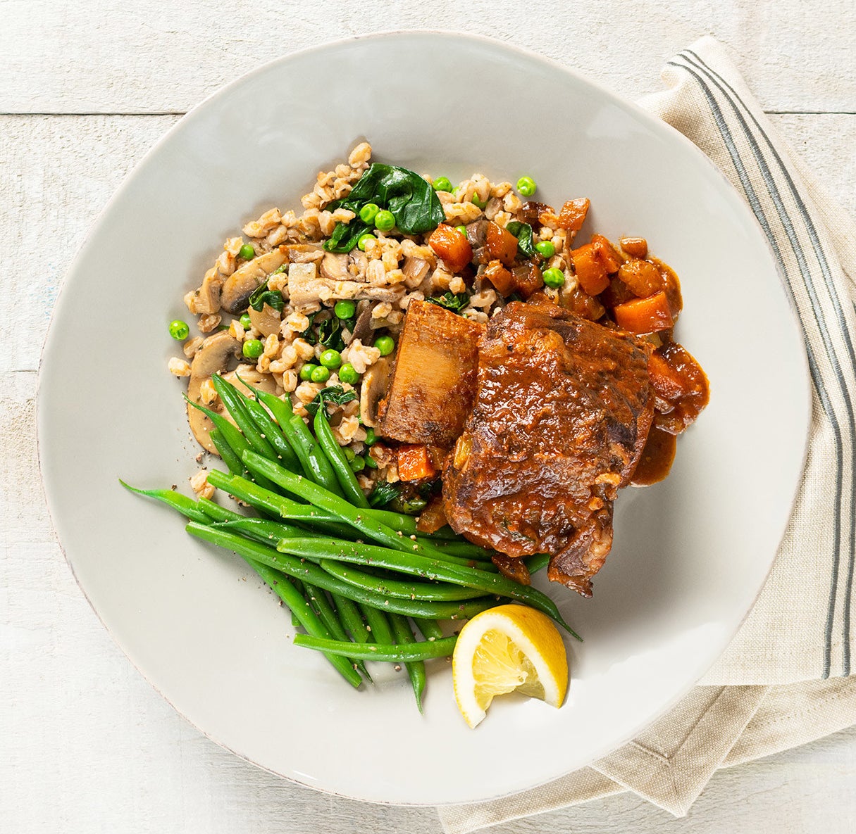 A top down view of the braised short ribs nestled on a bed of farro pilaf and steamed green beans