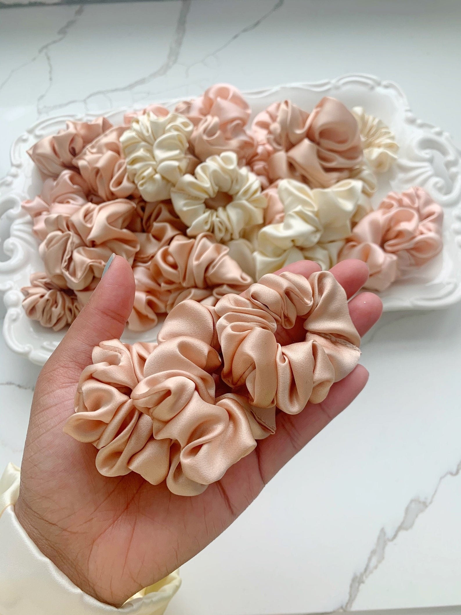 a model holding a handful of satin blush scrunchies