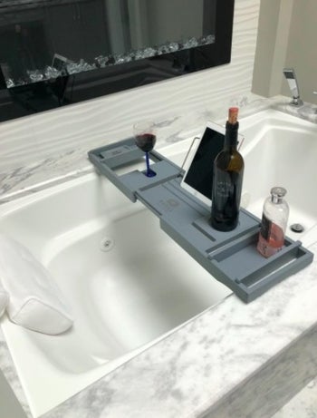 reviewer's bath caddy with a wine bottle and accessories on it 