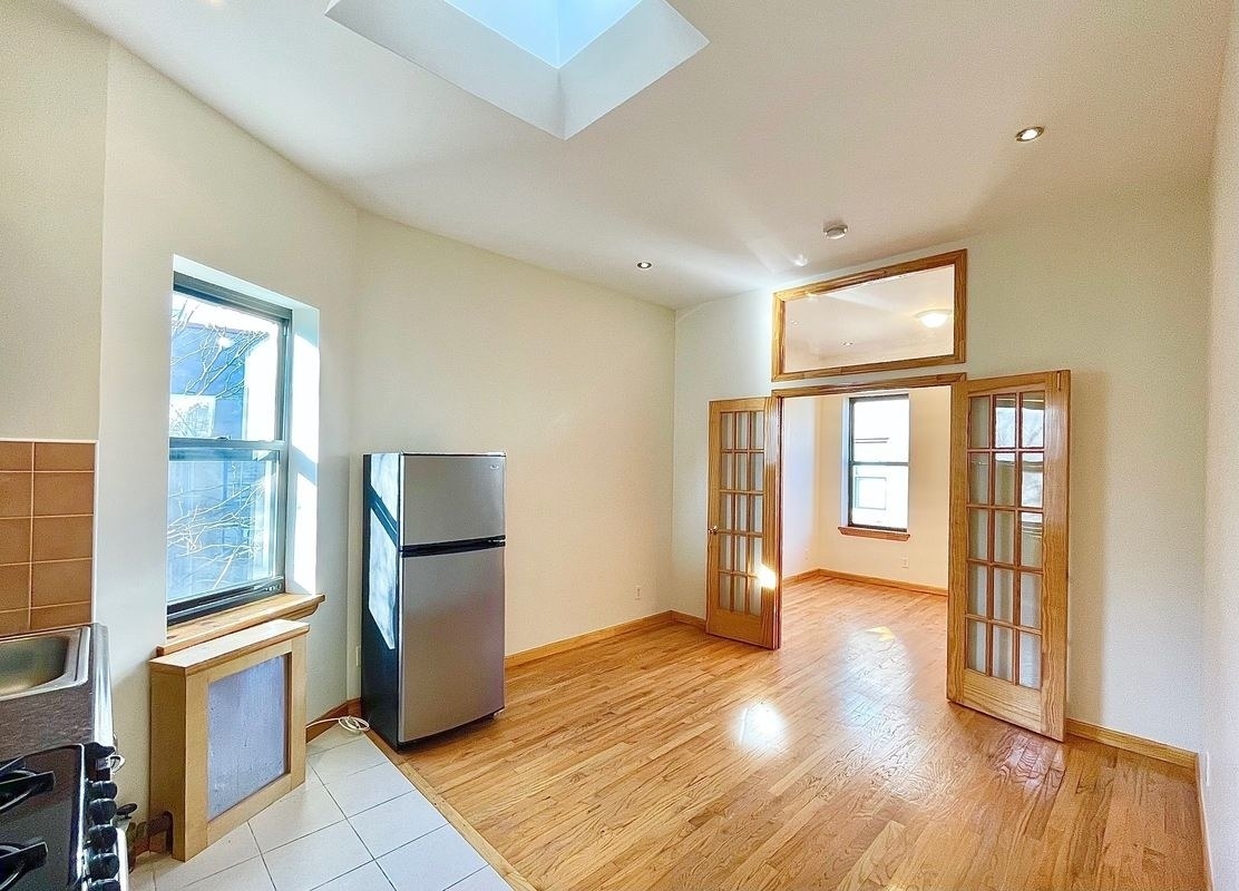 An open concept apartment with a stainless steel fridge, wood floors, gas stove, and double doors leading into another room