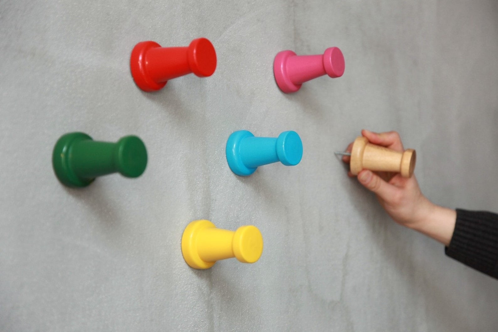 Model inserting one of the pin hooks into a wall next to five others in different colors