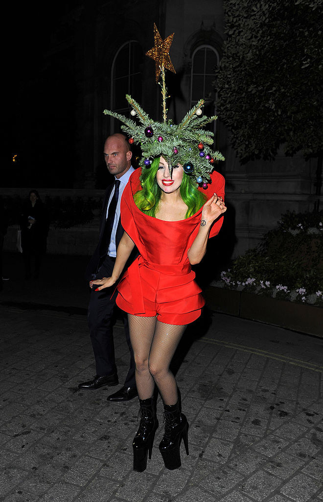 Lady Gaga wearing a red dress, green wig, and part of a Christmas tree, star topper included, on top of her head