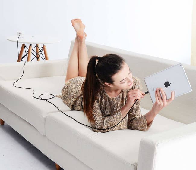 Model on couch plugging in 10-foot charger corn into iPad