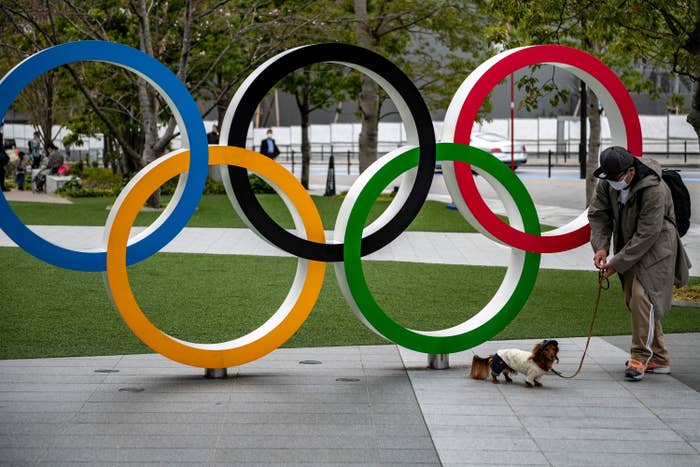 A man and his dog stands by a sculpture of the interlaced Olympic rings