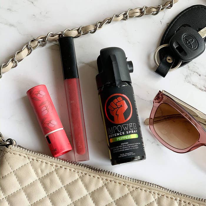 Pepper spray kept on a surface alongside other items in a woman’s purse, such as keys, lipstick, glasses, etc.