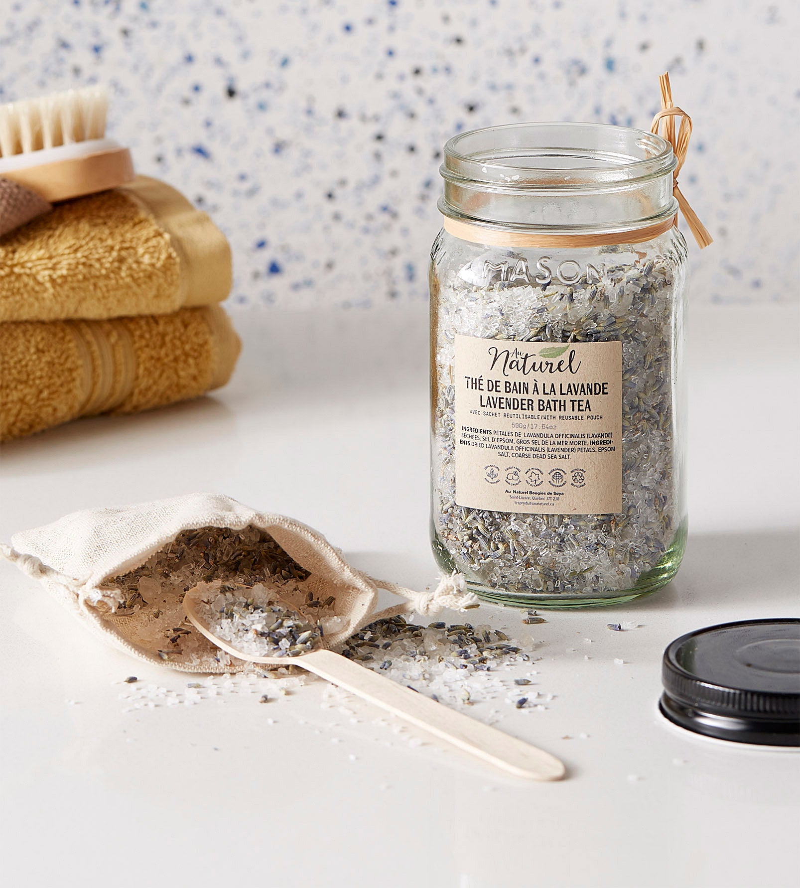 A large jar filled with bath salts There is a small wooden spoon next to the jar