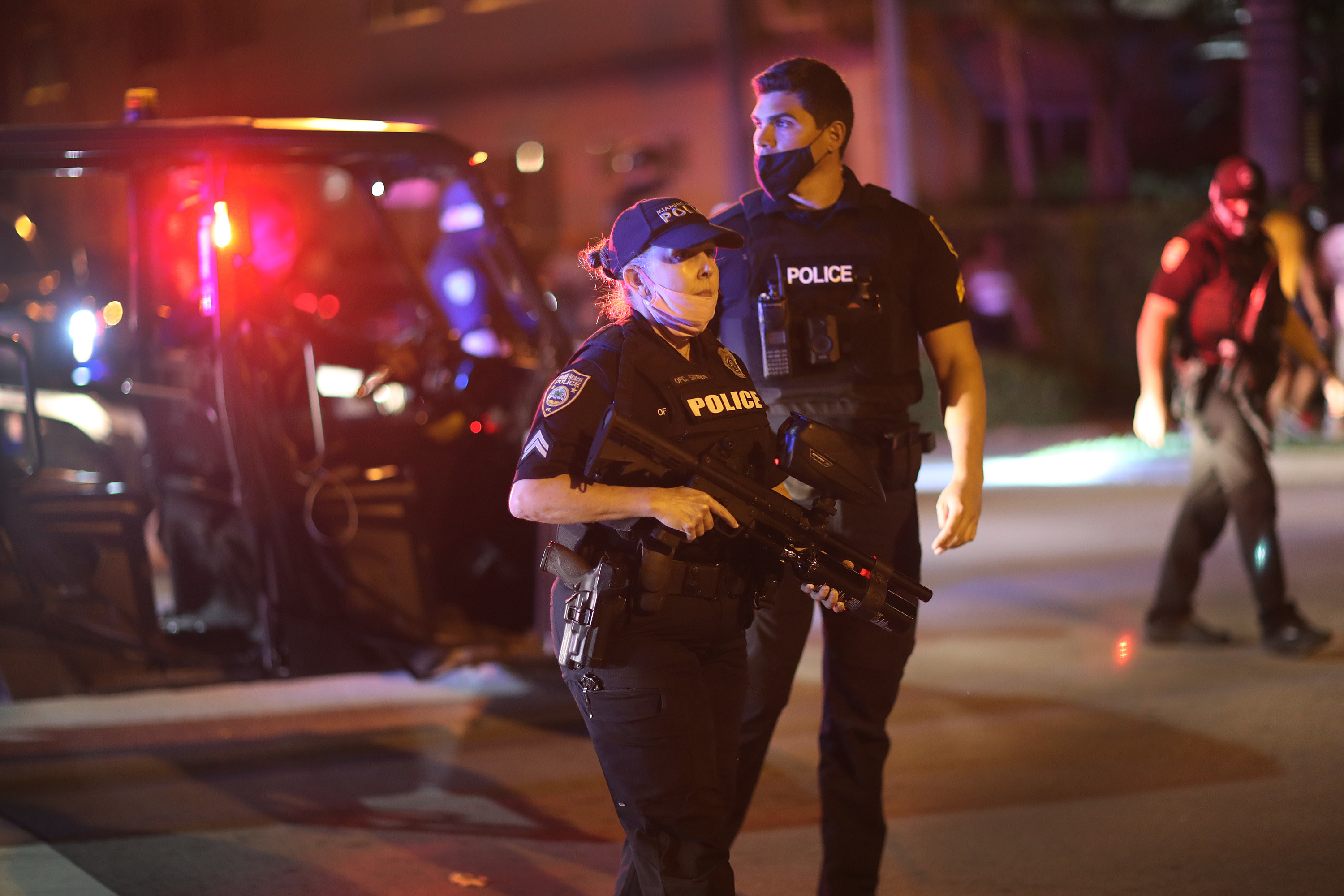 Two cops in tactical gear carrying tear gas launchers stand on the street