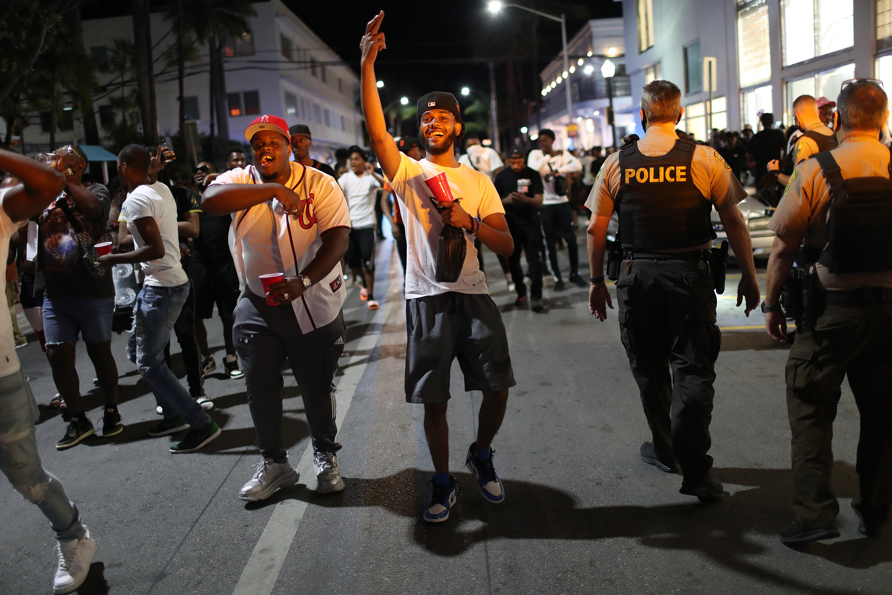 A group of guys with red solo cups wave as a group of cops walks by 