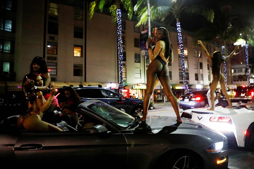 Women wearing swimsuits pose on top of sports cars at night