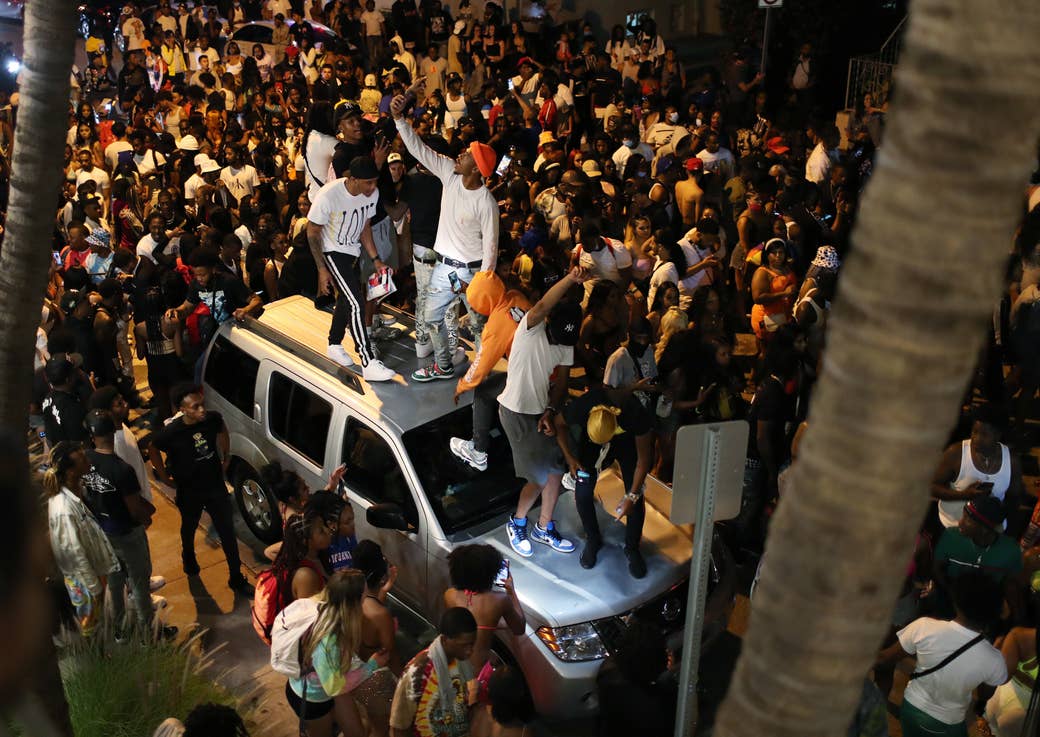 A group of guys on top of a car on a crowded street