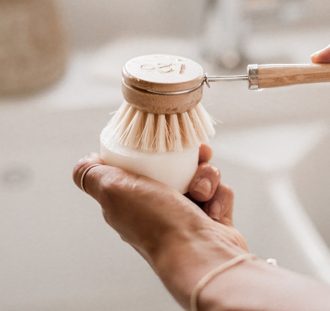 A person rubbing a dish brush on the solid washing bar