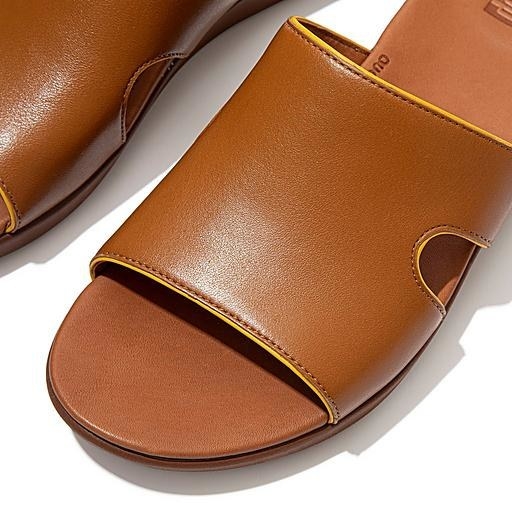 The sandal, which has a flat bottom and a thick strap with a small, semi-circular cut-out on either side of the mid-foot, in light tan