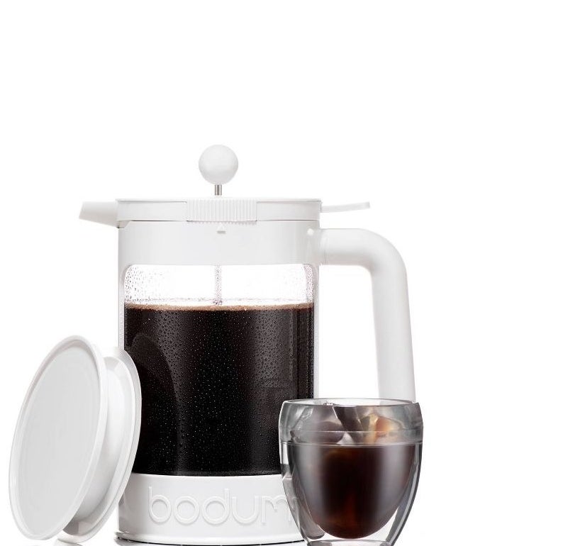 white french press style cold brew maker filled with coffee and next to a glass of iced coffee