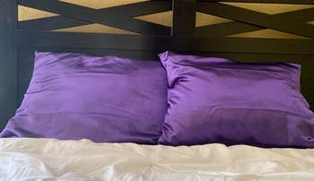 a reviewer photo of two pillows with purple satin pillowcases