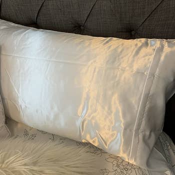 a reviewer photo of a white satin pillowcase on a bed 