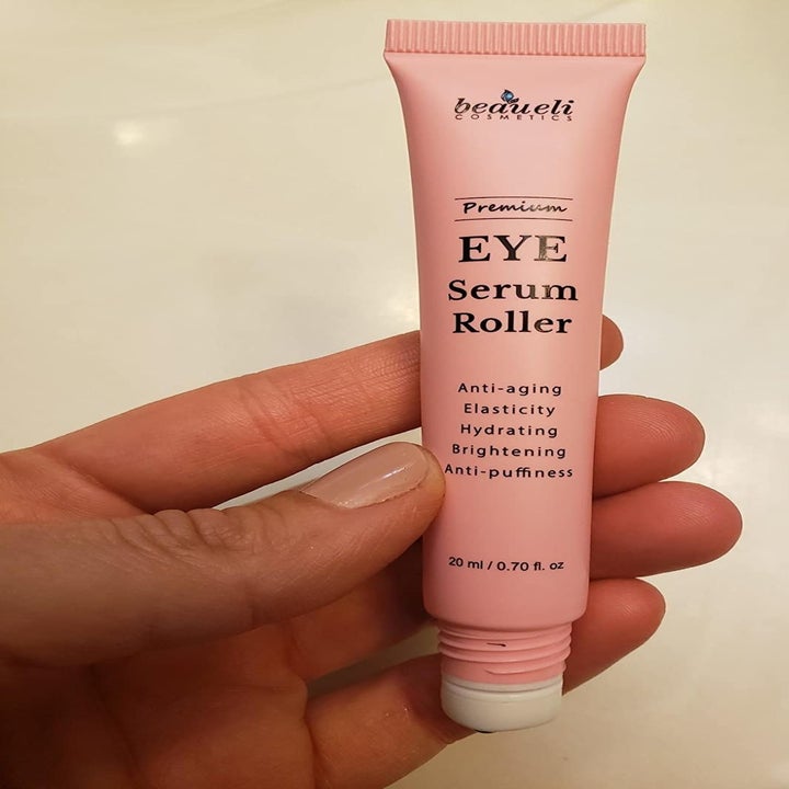 A reviewer photo of a hand holding the pink eye serum roller 